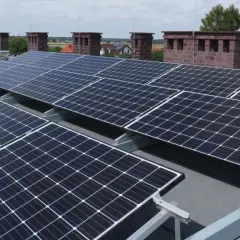 Solidna konstrukcja PV na dach płaski, z panelami ustawionymi pod optymalnym kątem do słońca. W tle kominy i zabudowania.
